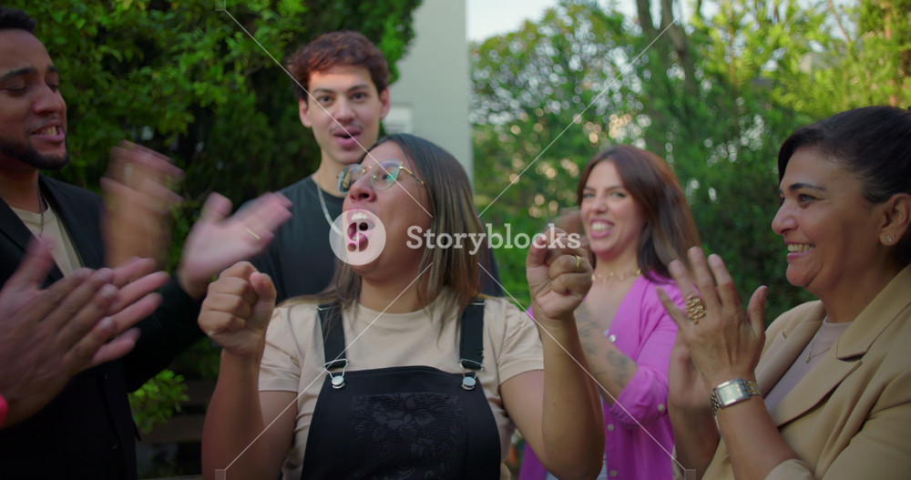 Latina woman celebrating at center of group as friends applaud her outdoors, expressing joy and excitement during heartfelt moment of recognition and support