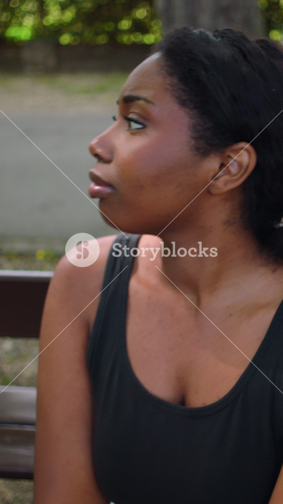 Young African American Woman seated on park bench showing visible stress and worry creating emotionally tense outdoor lifestyle atmosphere focused on anxiety pressure