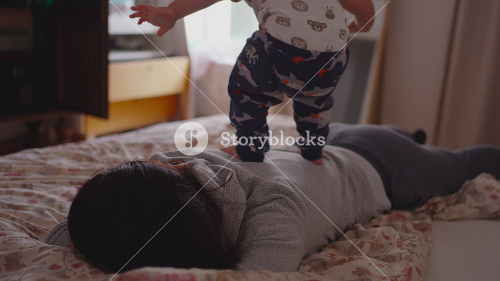 Toddler trying to stand up on mothers back during playful morning moment showing authentic childhood energy, warm family closeness, and lively early-day movement