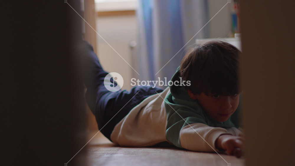 Young boy lying on bedroom floor at home looking bored and disengaged, highlighting childhood downtime, quiet moments, contemplation and everyday family life