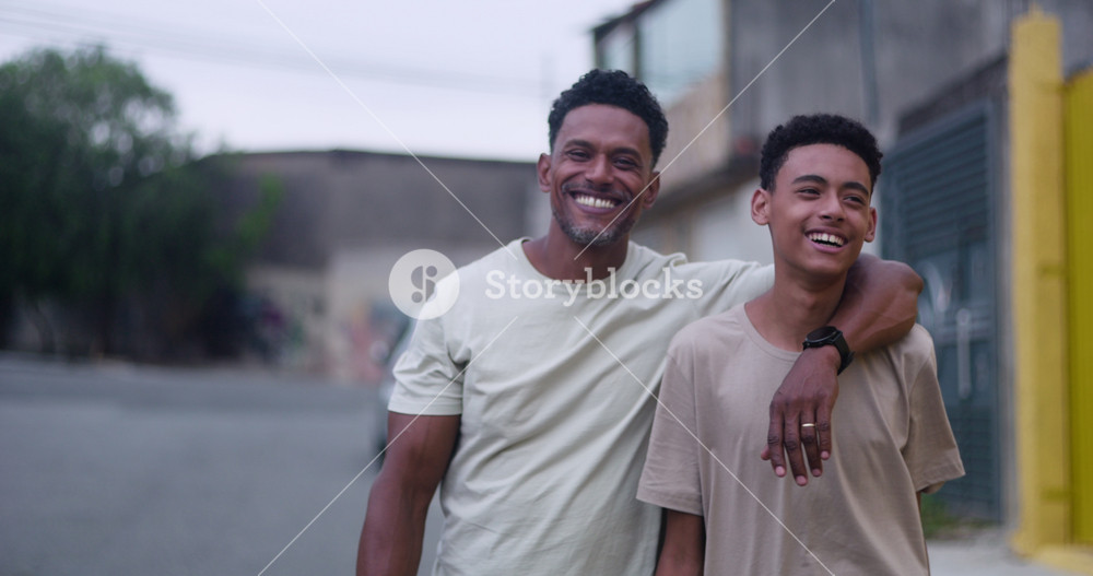 Smiling father of African descent with arm around son, sharing a moment of connection on a quiet street, outdoor bonding between father and teenage son in an urban setting