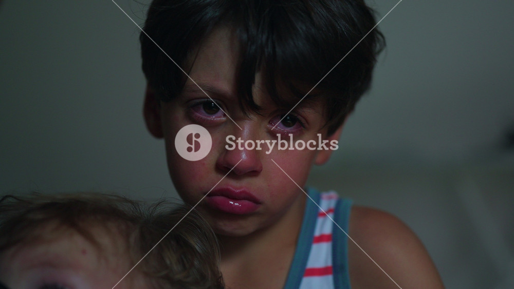 Close up of young boy with tearful eyes and sad expression holding younger sibling showing emotional childhood moment and protective brother bond inside family home