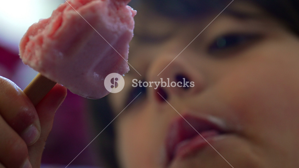 Macro close-up of child biting strawberry ice cream bar, highlighting frozen dessert, summer refreshment and carefree childhood