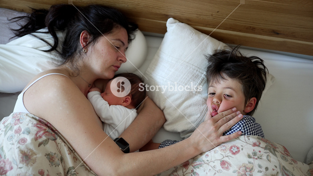 Mother and her two children in bed, newborn baby nestled in mom's arms, young child awake and playful, morning family time, warm and loving embrace, intimate moments, cozy home environment