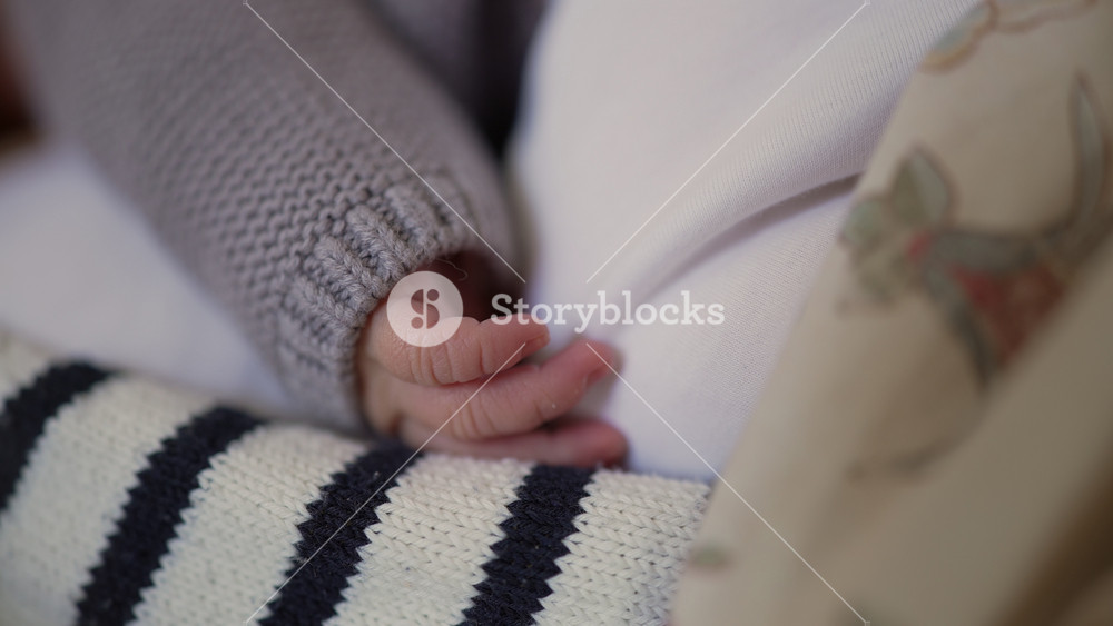 Close-up of a newborn’s hand resting gently on mother’s striped sweater, illustrating the delicate touch and connection between mother and child. a moment of tender care