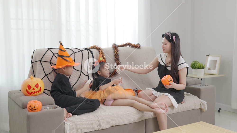Asian family celebrating Halloween at home, children dress in spooky costumes with mother, playing with festive