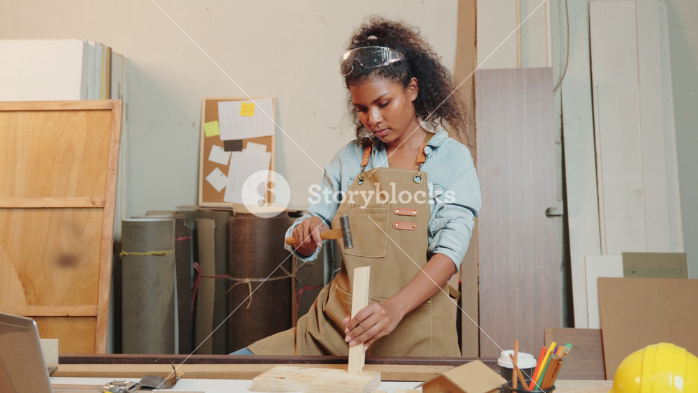 African American carpenter woman hammering a piece of wood for a chair in a woodworking shop. Skilled in crafting wooden