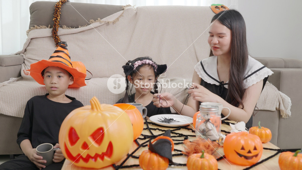 Asian family enjoying Halloween celebration, children decorating house for party, happy kids wearing costumes playing
