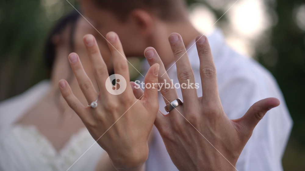 Bride and groom kiss while proudly showing wedding ring and diamond to camera. A tender and emotional moment full of love and happiness on