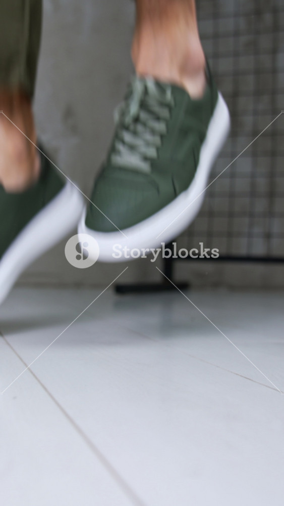 Man in khaki jeans and sneakers jumps demonstrating comfortable sport shoes. Close up. Fashionable stylish footwear presentation in studio. Vertical video