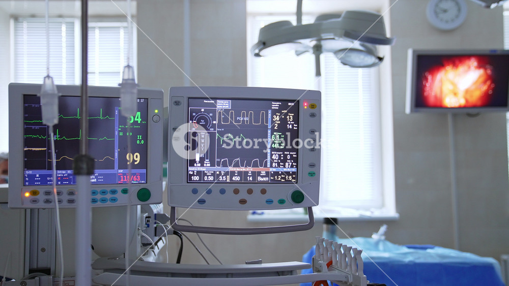 Well-equipped surgical theatre. Screens and monitors showing patient's vital signs and operated area by the robotic equipment.