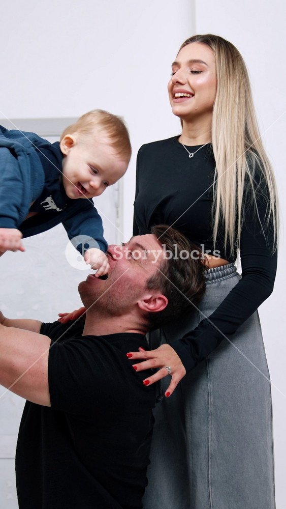 Caring and loving Caucasian parents play with their beloved baby. Father lifts his son with one hand and mom kisses the child.