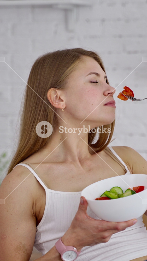 Young woman eating salad. Beautiful girl sniffing and eating organic vegetables on the kitchen background. Natural food concept. Vertical video