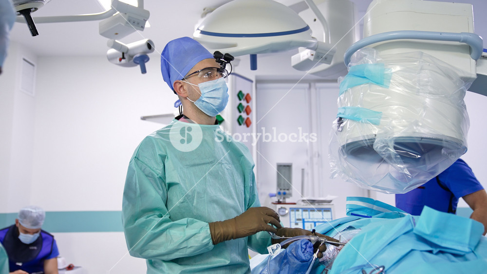 Kyiv, Ukraine, 5 May 2022: Medical professional uses surgery instrument for neurosurgical operation. Doctor watches the screen to conduct the operation. Team of surgeons in modern hospital.