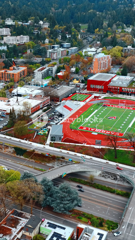 Lively multi-lane highway with bridges above. Green stadium of school in the scenery of Portland, Oregon, the USA. Lots of greenery at backdrop. Vertical video
