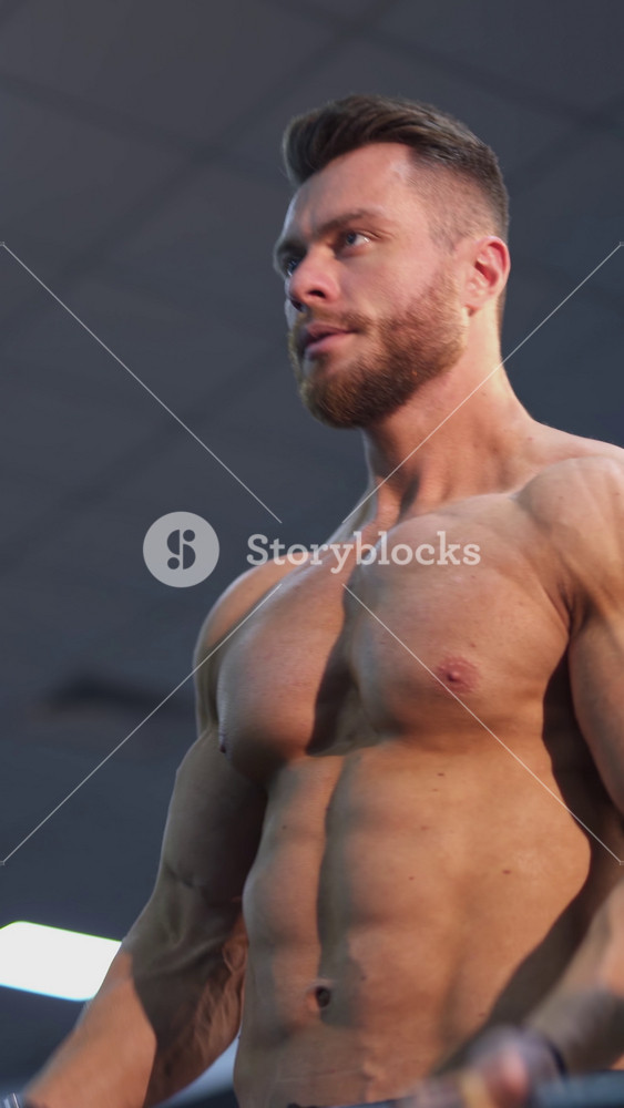 Shirtless athlete pumping muscles with a barbell. Sportsman doing weightlifting exercise in fitness gym. Healthy lifestyle. Close-up. Vertical video