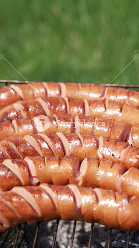 Tasty fried sausages on a grill. Grilled sausages with incisions ready to eat for a picnic. Hot dog sausages roasting in charcoals outdoors. Barbeque. Vertical video