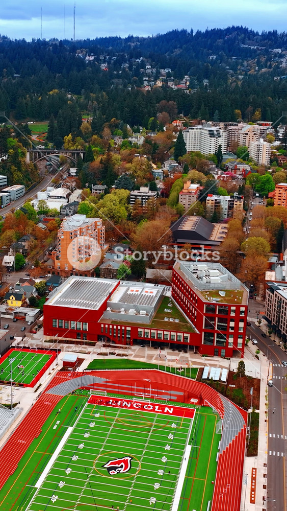 Bright cityscape of Portland, Oregon, the USA with school stadium in center. Hills overgrown with pine trees at backdrop. Top view. Vertical video