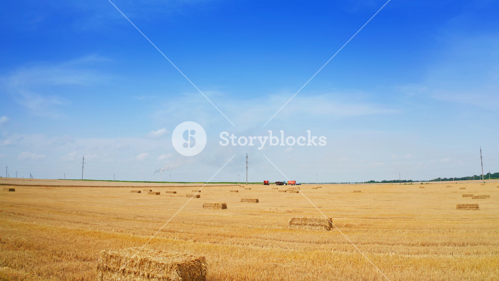 Contrasting blue sky with yellow field of mowed wheat and hay bales on. Fast approaching to the agricultural machinery standing in the field.