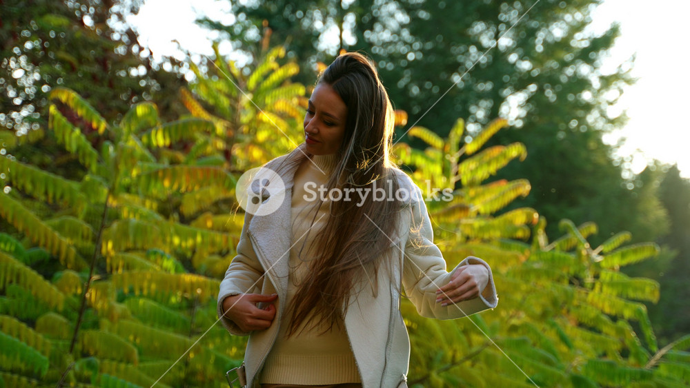 Beautiful young woman waving her long gorgeous dark hair in the rays of sun. Lady enjoying amazing autumn day in the park.