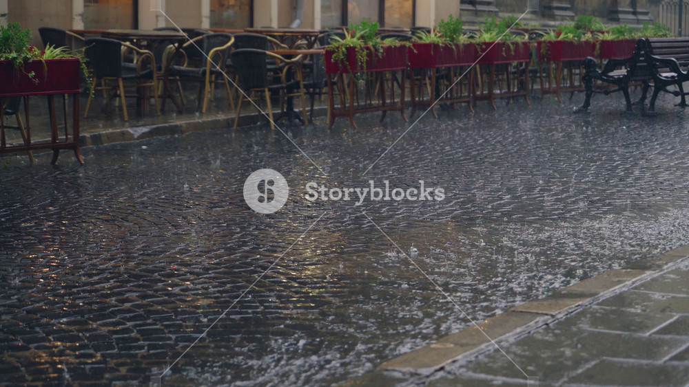 stream of water are flowing through the pavement in rainy weather. Raindrops is falling on the road against the background of the summer terrace of the restaurant