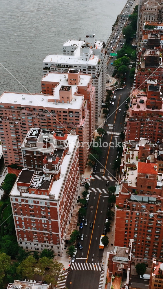 Residential multistoried buildings above the river. Busy traffic on the roads of New York at daytime. Top view. Vertical video