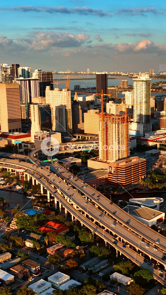 Bright light of setting sun illuminating the skyscrapers in the uptown of Miami, Florida, USA. Drone rising above the beautiful city with lively traffic. Vertical video