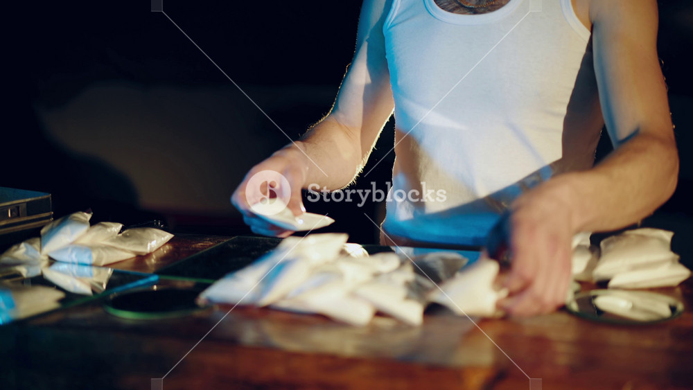 Drugs. In the underground laboratory drug dealer places brick packs filled with drugs Into the suitcase for further selling and distribution.
