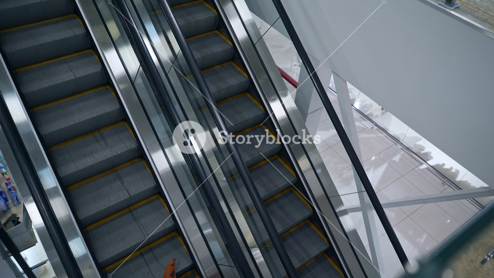 Person wearing inflatable orange costume of T-Rex animal steps on the escalator. Dinosaur with an open mouth rides down in the supermarket. Top view.