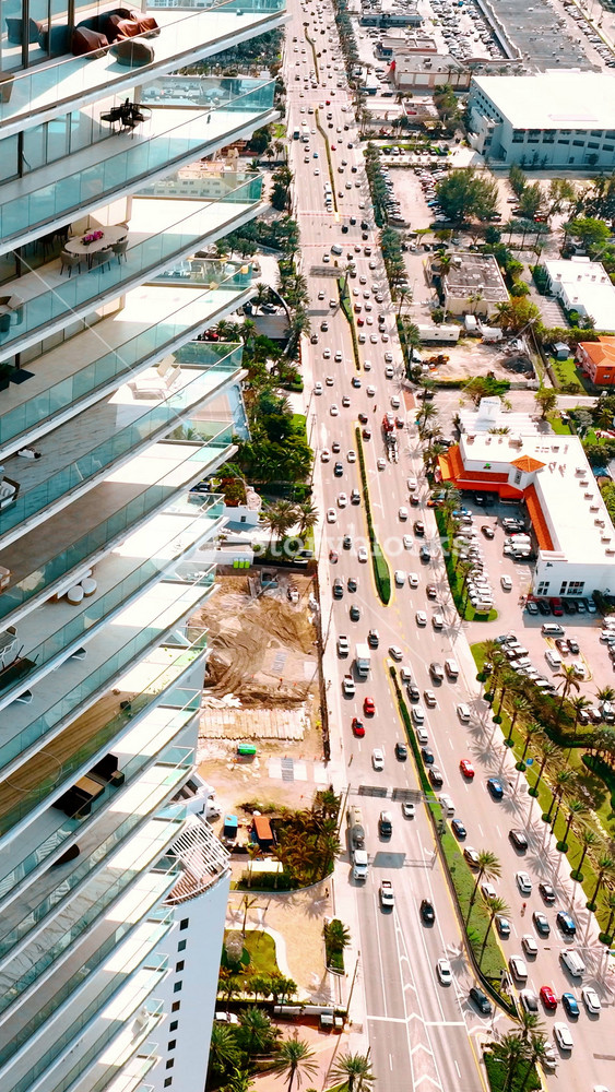 Rising along the multi-storied apartment block with large open balconies. Street with busy highway at the foot of the building. Top view on Miami Beach, Florida, USA. Vertical video