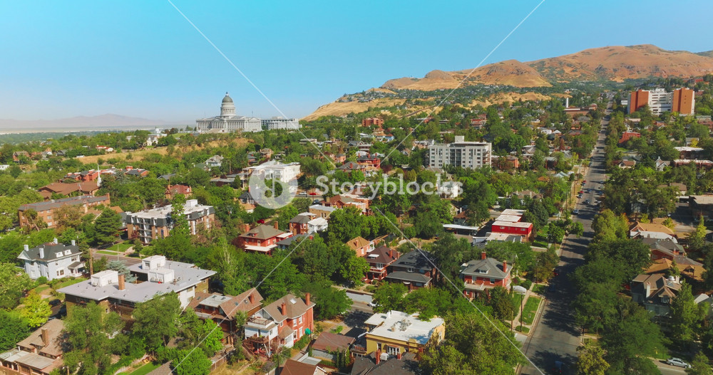 Beautiful sunny city built near the bare mountain. Magnificent State Capitol Building at the foot of rock. Salt Lake City panorama on clear summer day.