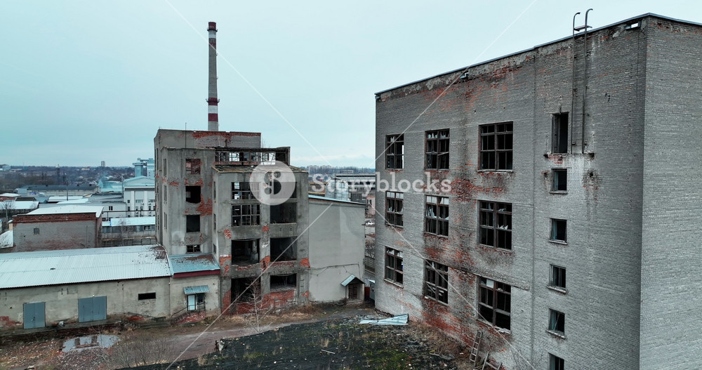 Damaged ruins of past big plant. Forlorn wrecked emptied buildings with no windows and old brick walls. Blue clear sky at the background.