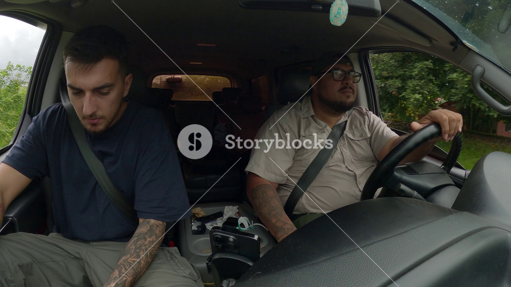 Two male friends talking and smiling inside a car during a road trip adventure through the lush green landscape of Costa Rica