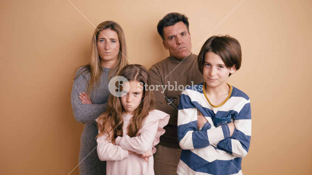 Comical family of four standing together with crossed arms and making funny, angry faces. Mother, father, son, and daughter joking around