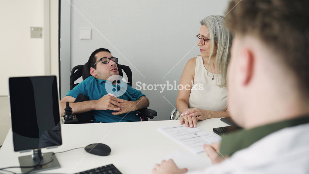 Man with spina bifida in a wheelchair talking with his doctor in the hospital. His mother is assisting him during the medical consultation