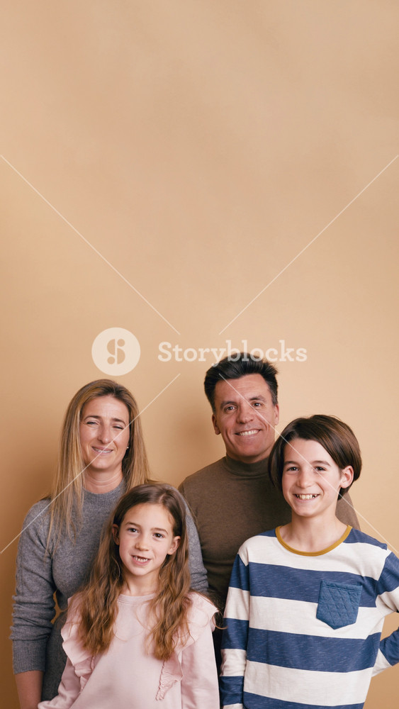Cheerful family with son and daughter smiling and looking at the camera. Parents and children standing together against a beige background