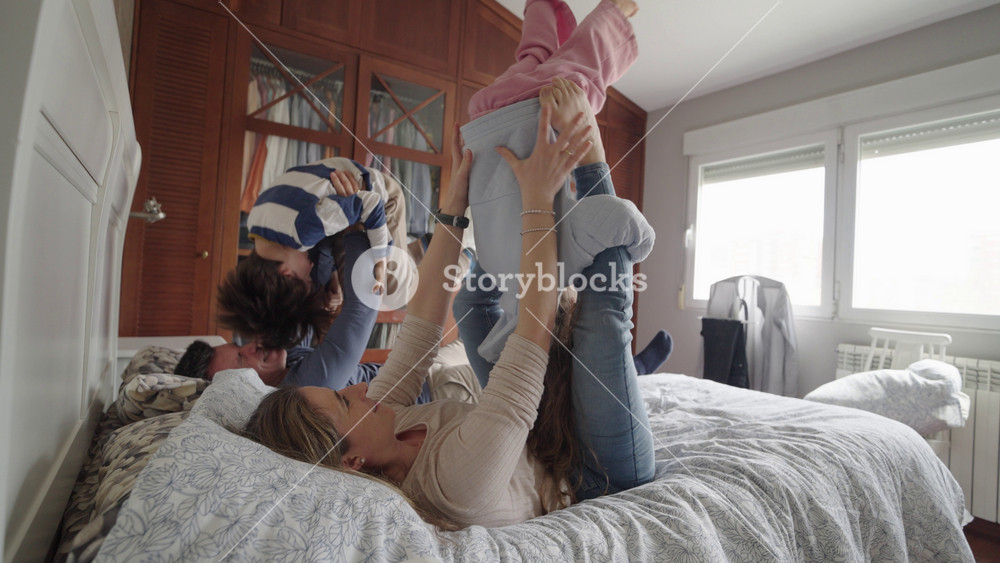Family members joyfully playing, jumping, and laughing together on bed in bright, cozy bedroom, sharing genuine moments of happiness and