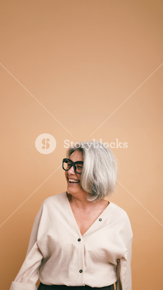 Joyful and stylish elderly woman with grey hair and fashionable glasses laughing uncontrollably, expressing genuine happiness and amusement