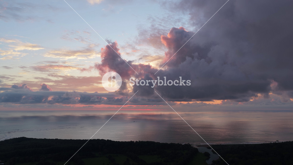 Stunning aerial view of a vibrant sunset over the Pacific Ocean. Colorful clouds reflect on the calm water near the tropical coast of Uvita