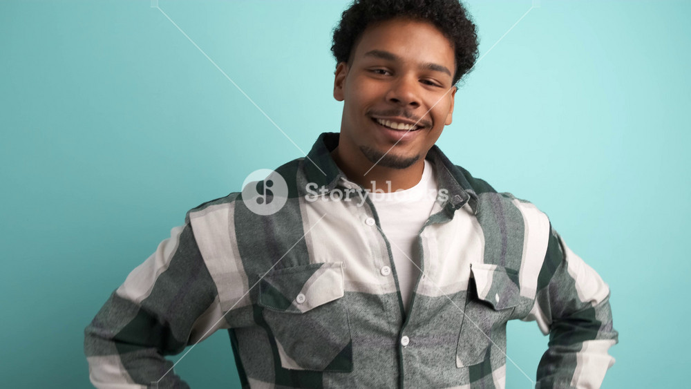 Portrait of happy young Brazilian male with afro hair in shirt looking at camera and winking against blue background