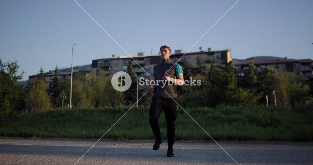 Man jogging along the road near residential buildings in the evening light promoting fitness and outdoor activity