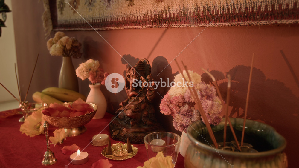 No people warm light shot of incense sticks placed in vase smouldering on home hindu altar near flowers, Ganesh statue and traditional religious decor on table