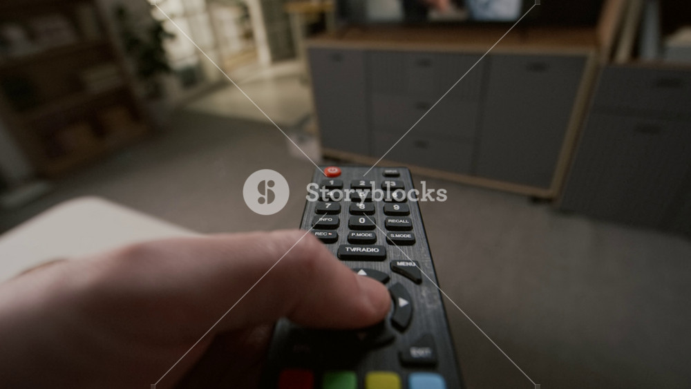 POV close-up of male hand holding remote control, pressing button, unable to turn off TV set, while love drama is played on screen, of man and woman having violent argument and fighting
