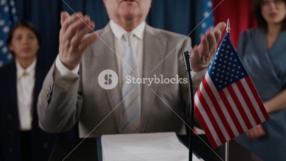 Portrait of senior politician speaking at podium with American flag and gesturing during press conference. Clip is ideal for political campaigns, news broadcasts, and government videos, close up shot