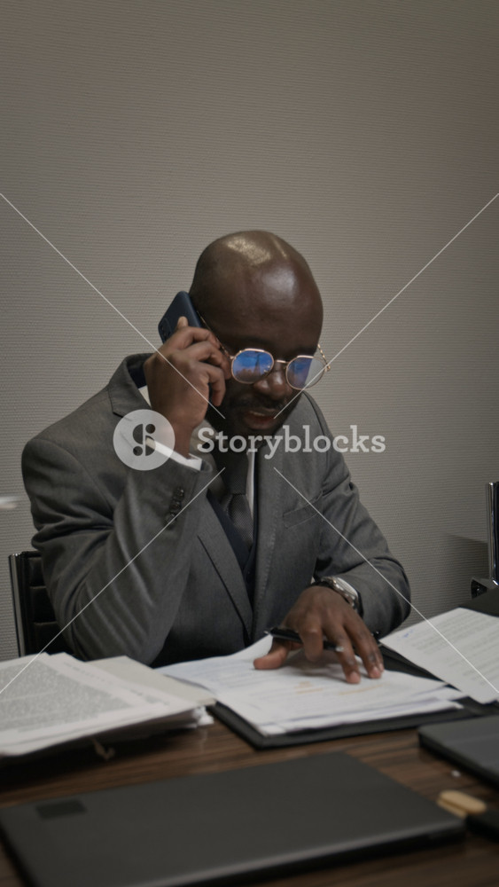 Medium vertical shot of nervous, frustrated African American male lawyer arguing with colleague on mobile phone, complaining over mistakes in document late at night, loosening neck tie