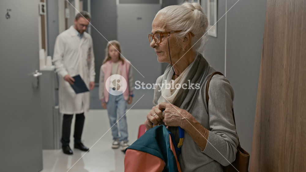 Side view shot of grandmother waiting for child in clinic hall with doctor and girl walking into shot smiling and talking