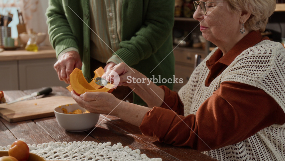 Senior Caucasian woman scraping seeds from pumpkin slice with spoon while senior man assists. Clip is ideal for senior lifestyle, retirement hobbies, and autumn cooking commercials