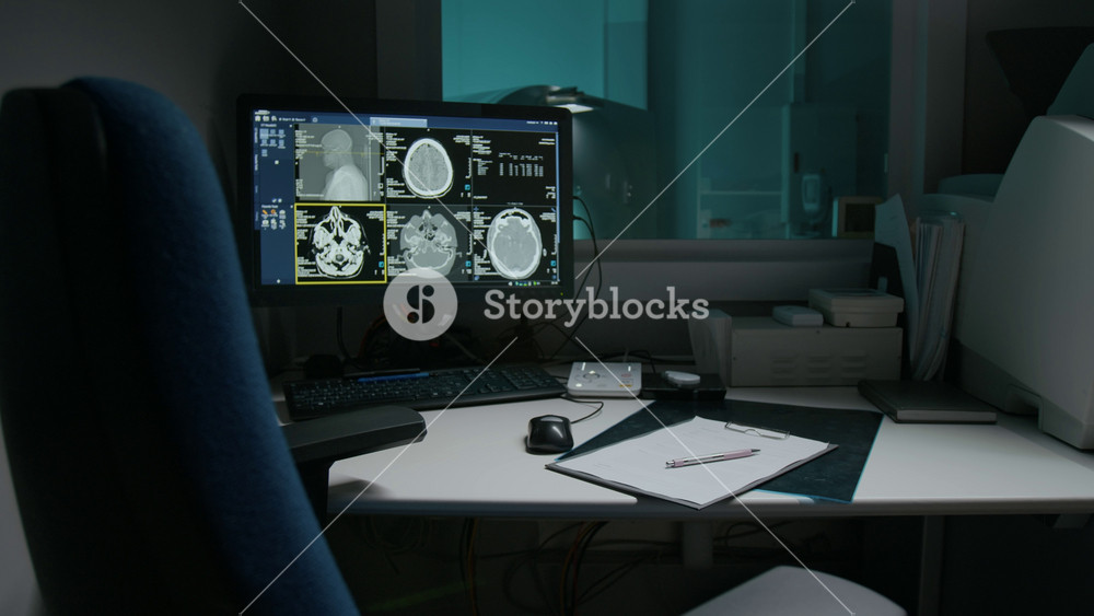 Full no people shot of patient brain scan on computer screen on desk of tomography specialist at neurosurgery clinic, after workday or at night. MRI machine behind glass window in blue light