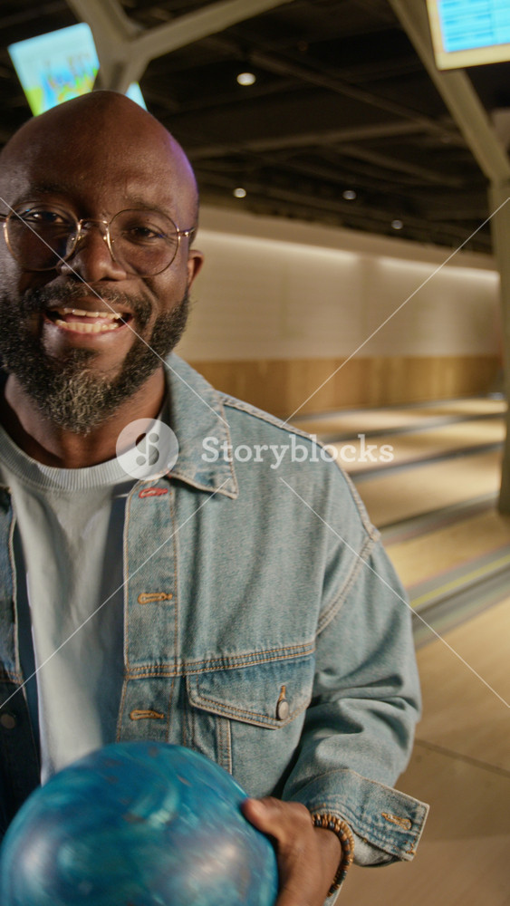 POV of young African American man throwing bowling ball and celebrating strike with diverse friends, recorded on smartphone for social media. Video suits leisure and friendship promotions, vertical
