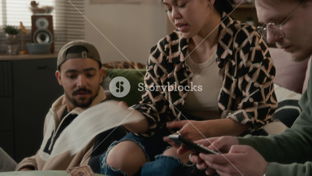 Diverse young students sitting in living room, reviewing bills, Hispanic girl counting cash, and expressing frustration over high household expenses. Personal finance apps or banking advertisements